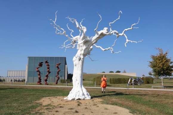 Die Skulptur autumn moon des Künstlers Ugo Rondinone vor dem Museum Würth 2 in Künzelsau. Es handelt sich um einen lebensechten künstichen blätterlosen weißen Baum der seine knorrigen Äste gen Himmel streckt. In Hintergrund sind weitere Skulpturen des Skulpturengartens zu sehen. 